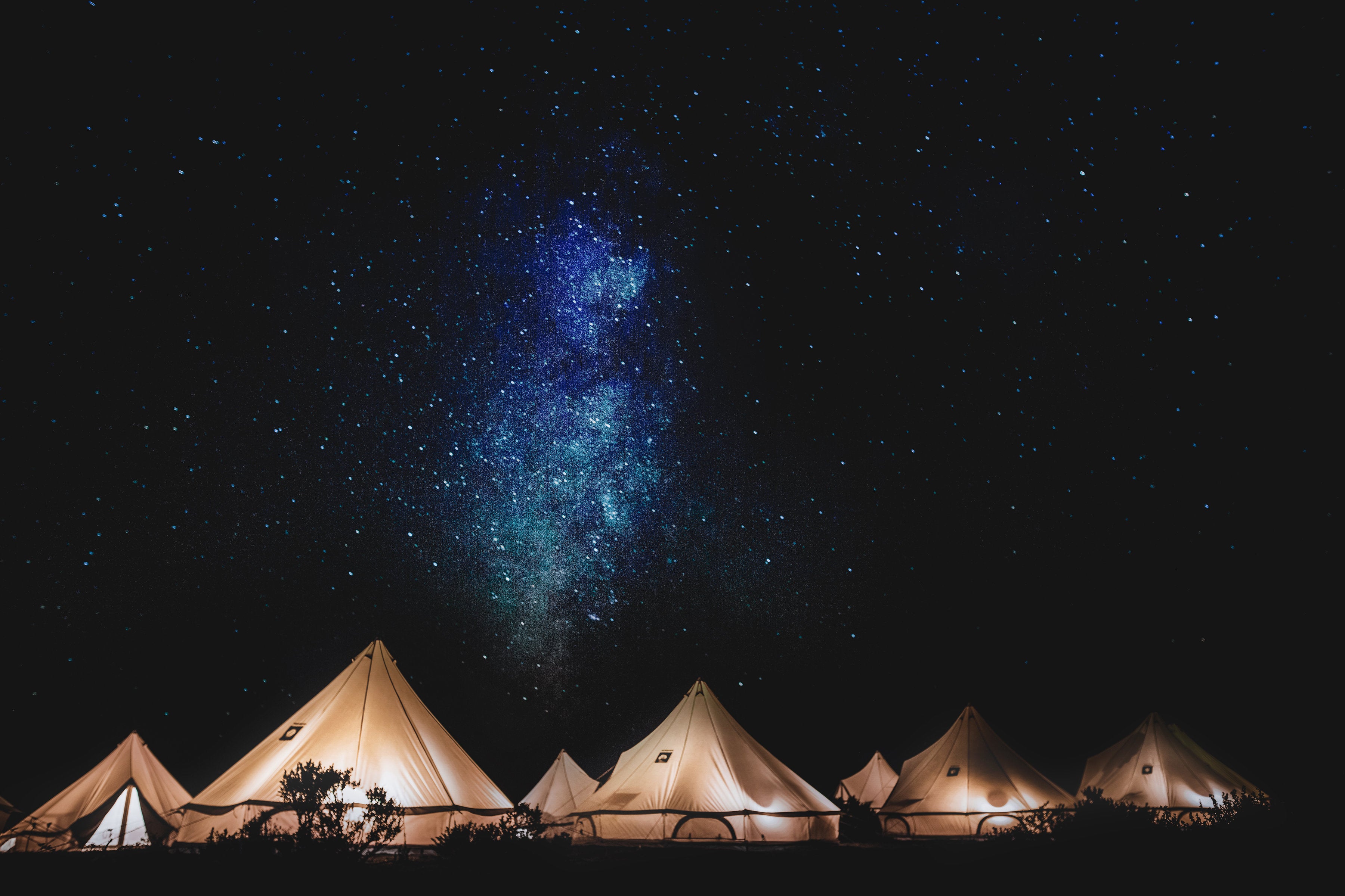 Starlit night sky over a row of illuminated tents.