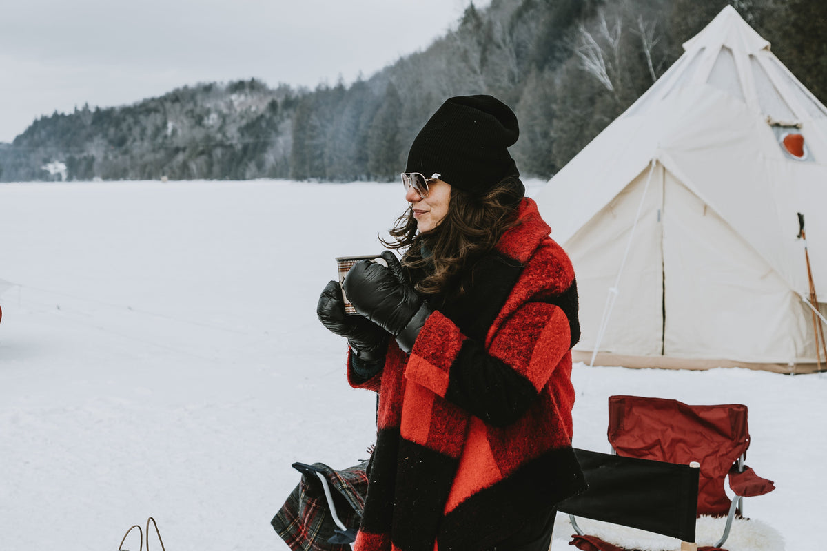 Two people in winter clothing standing in a snowy landscape with tents and camping gear.