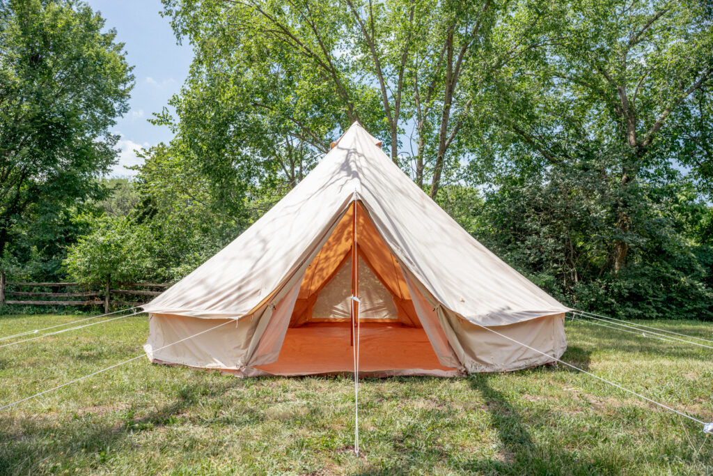 Exterior view of a 20ft 6M Pro Stout Bell Tent on a raised wooden platform in a forest clearing.